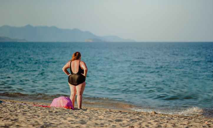 photography of a woman in black swimsuit standing on the seashore